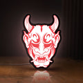 Front view of Cyberpunk Japanese Oni Mask Demon LED lightbox sign glowing on a wooden desk