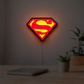 Superman S LED lightbox hanging on a room wall with soft red light