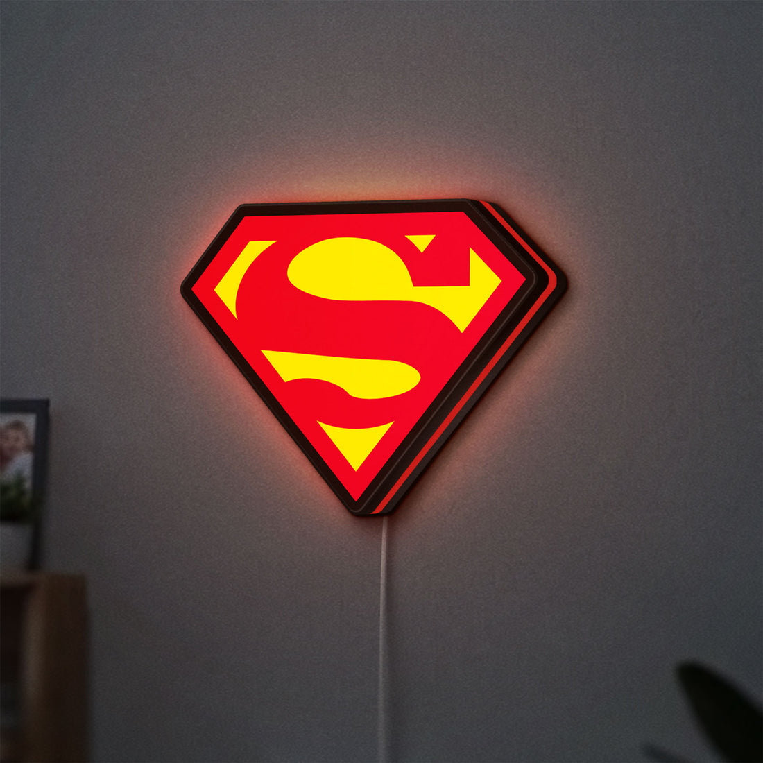 Superman S LED lightbox hanging on a wall with red glow