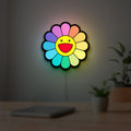 Takashi Murakami Rainbow Flower LED lightbox hanging on a room wall with soft yellow light