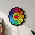 Unlit Takashi Murakami Rainbow Flower LED lightbox mounted on a wall in daylight