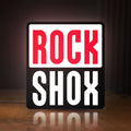 Front view of Rock Shox LED lightbox sign glowing on a wooden desk