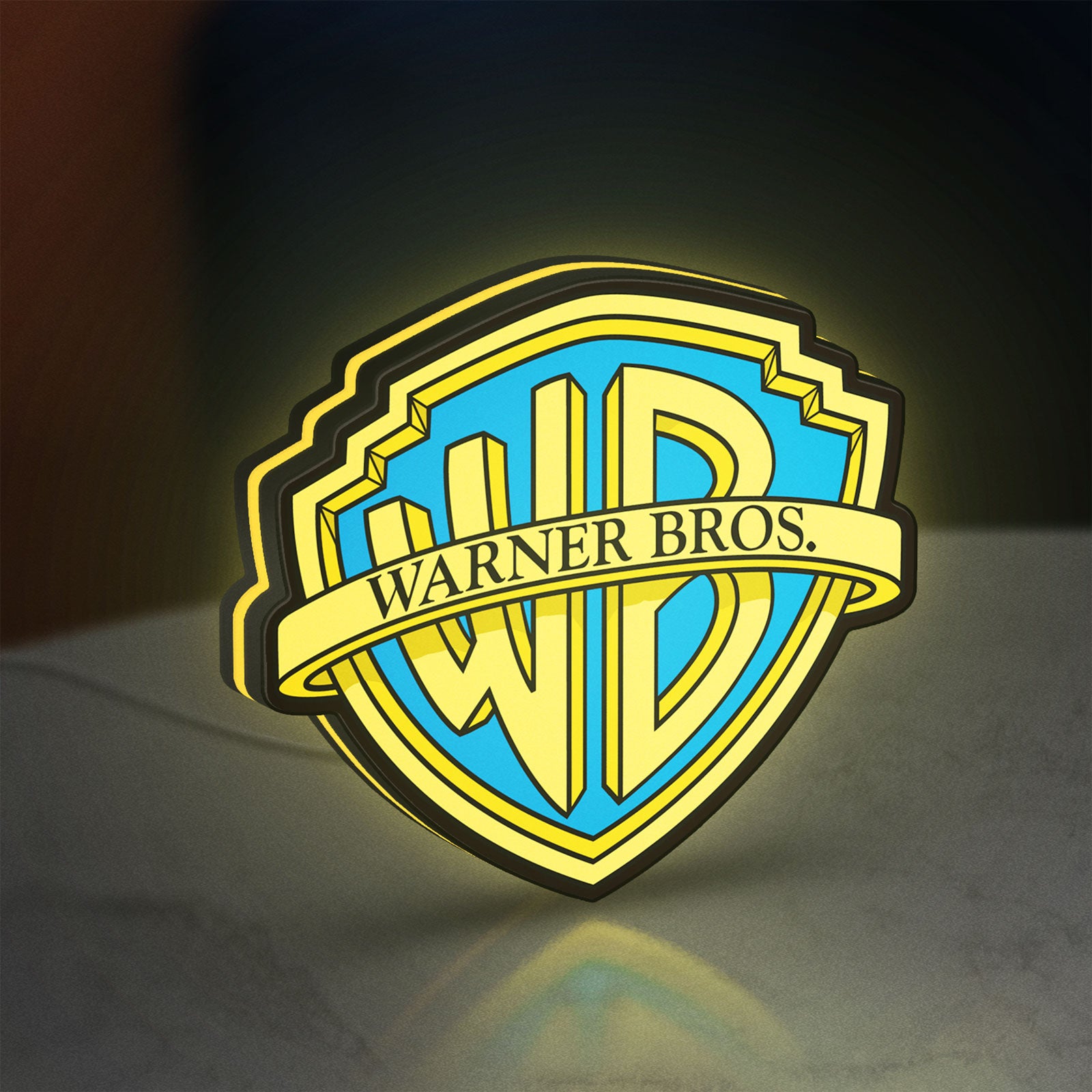 Warner Bros Shield LED lightbox standing on a desk from an angled side view with yellow glow