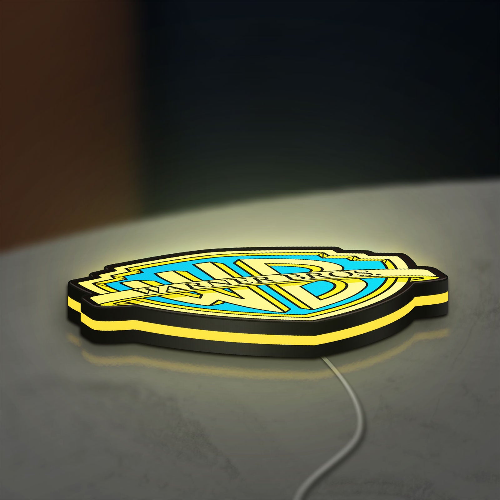 Warner Bros Shield LED lightbox lying flat on a desk with yellow glow