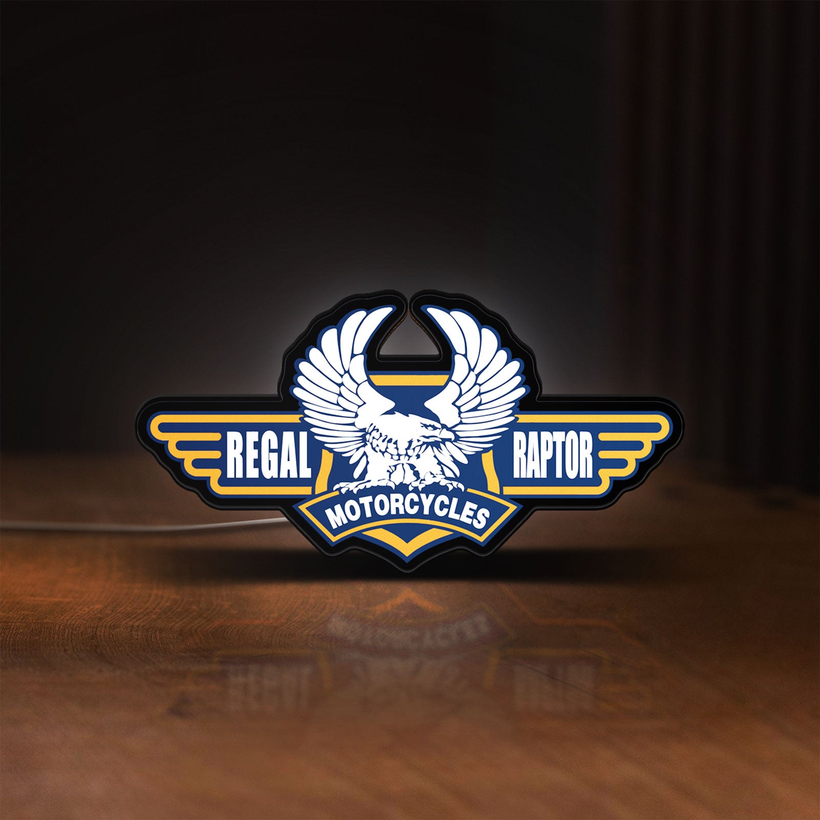 Front view of Regal Raptor Motorcycles LED lightbox sign glowing on a wooden desk