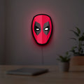 Deadpool Head LED lightbox hanging on a room wall with soft red light