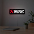 Akrapovic LED lightbox hanging on a room wall with soft red light
