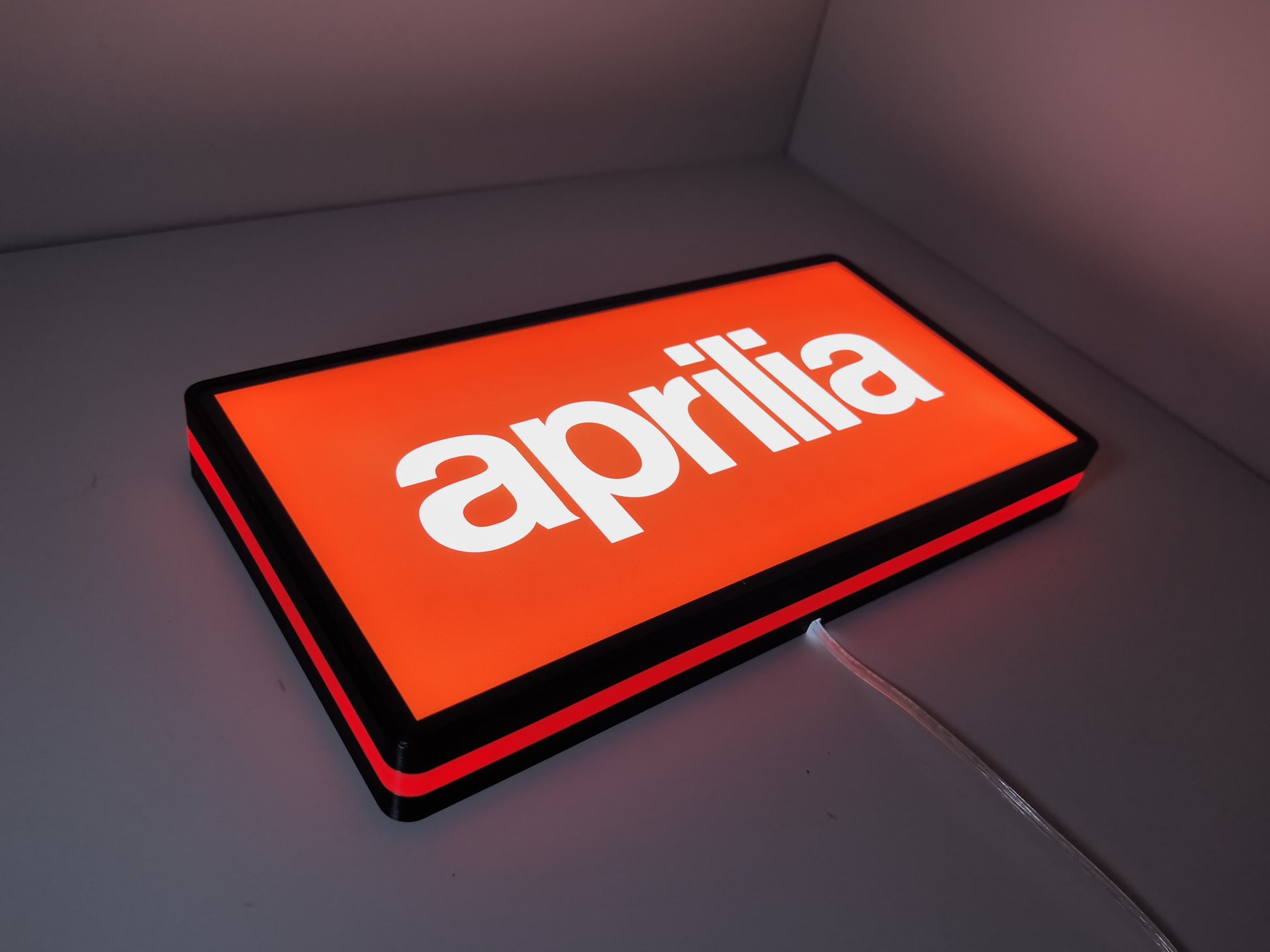 Illuminated flat lay angled view of Aprilia Dimmable Illuminated Sign in 30cm, unique wall art for desk and room decor