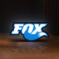Front view of Fox Racing Shox LED lightbox sign glowing on a wooden desk