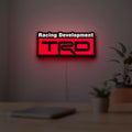 TRD Racing Development LED lightbox hanging on a room wall with soft red light