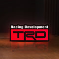 Front view of TRD Racing Development LED lightbox sign glowing on a wooden desk