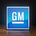 Front view of GM LED lightbox sign glowing on a wooden desk