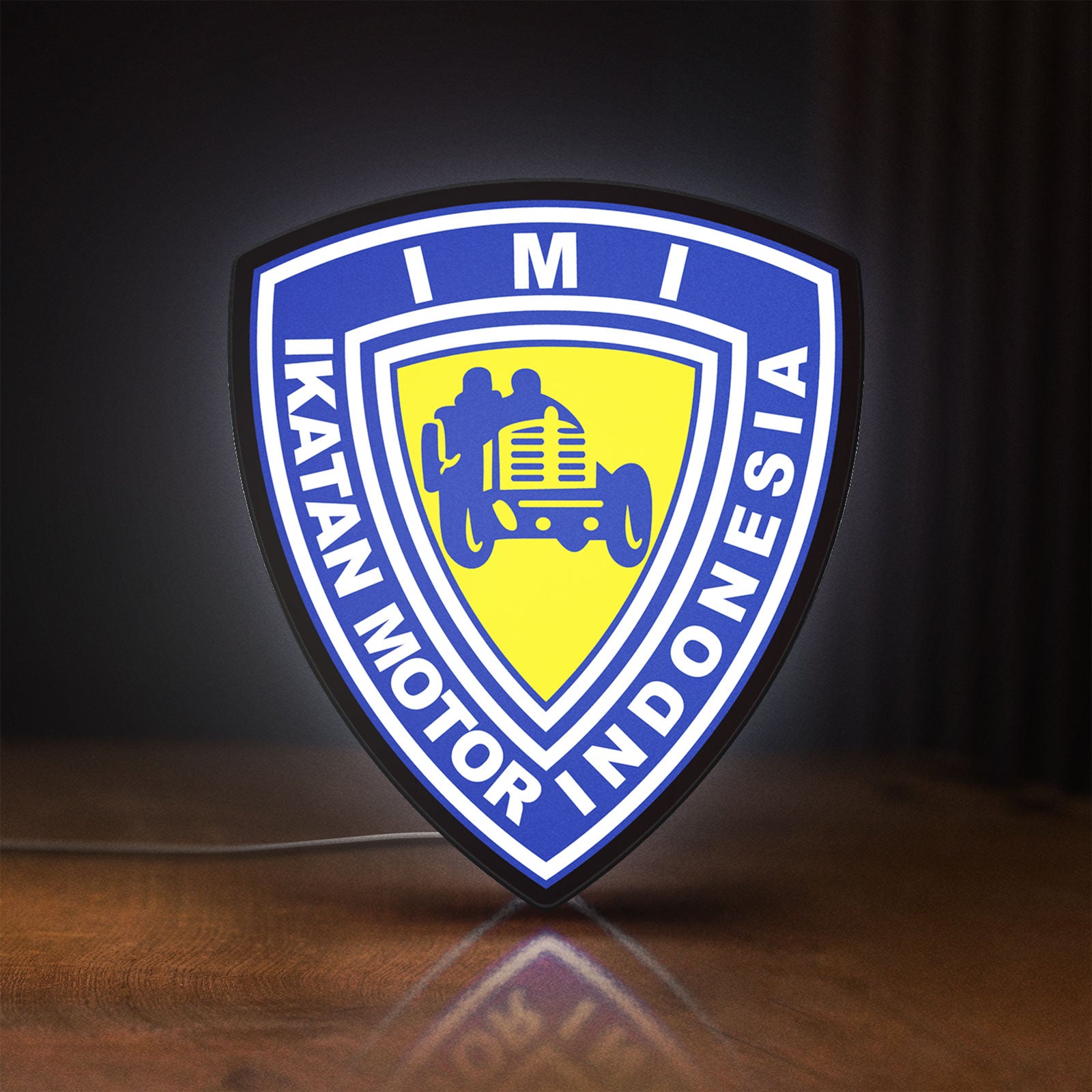 Front view of Ikatan Motor Indonesia LED lightbox sign glowing on a wooden desk