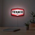 Texaco LED lightbox hanging on a room wall with soft red light
