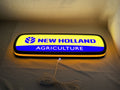 Illuminated flat lay angled view of New Holland Agriculture 3D LED Sign in 50cm, perfect for garage and man cave decor