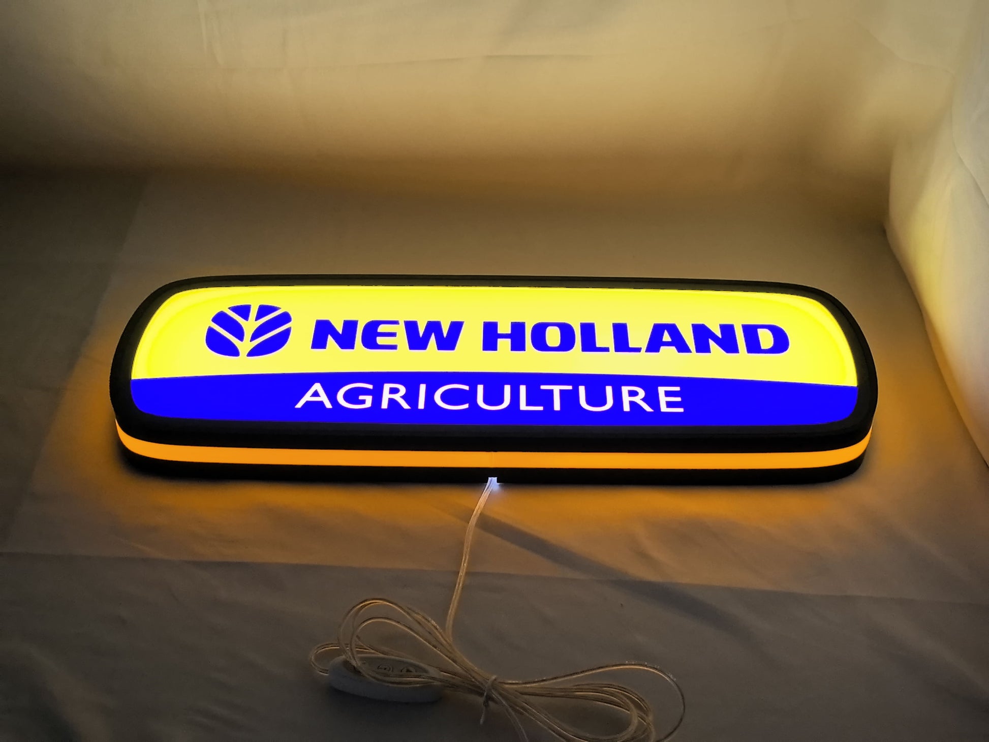 Illuminated flat lay angled view of New Holland Agriculture 3D LED Sign in 50cm, perfect for garage and man cave decor