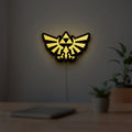 The Legend of Zelda Hyrulian Crest LED lightbox hanging on a room wall with soft yellow light