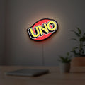 UNO Wild Draw Four LED lightbox hanging on a room wall with soft yellow light