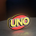 UNO Wild Draw Four LED lightbox standing on a desk from an angled side view with yellow glow