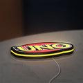 UNO Wild Draw Four LED lightbox lying flat on a desk with yellow glow