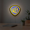Warner Bros Shield LED lightbox hanging on a room wall with soft yellow light