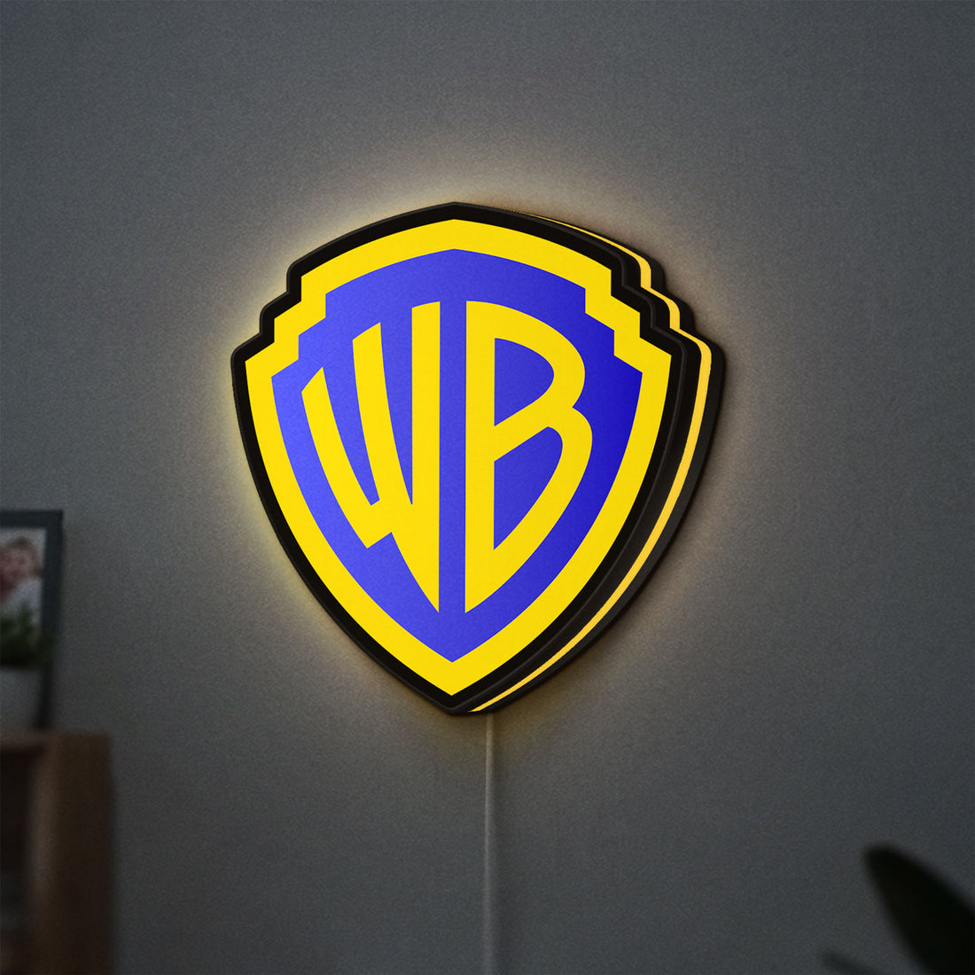 Warner Bros Shield LED lightbox hanging on a wall with yellow glow