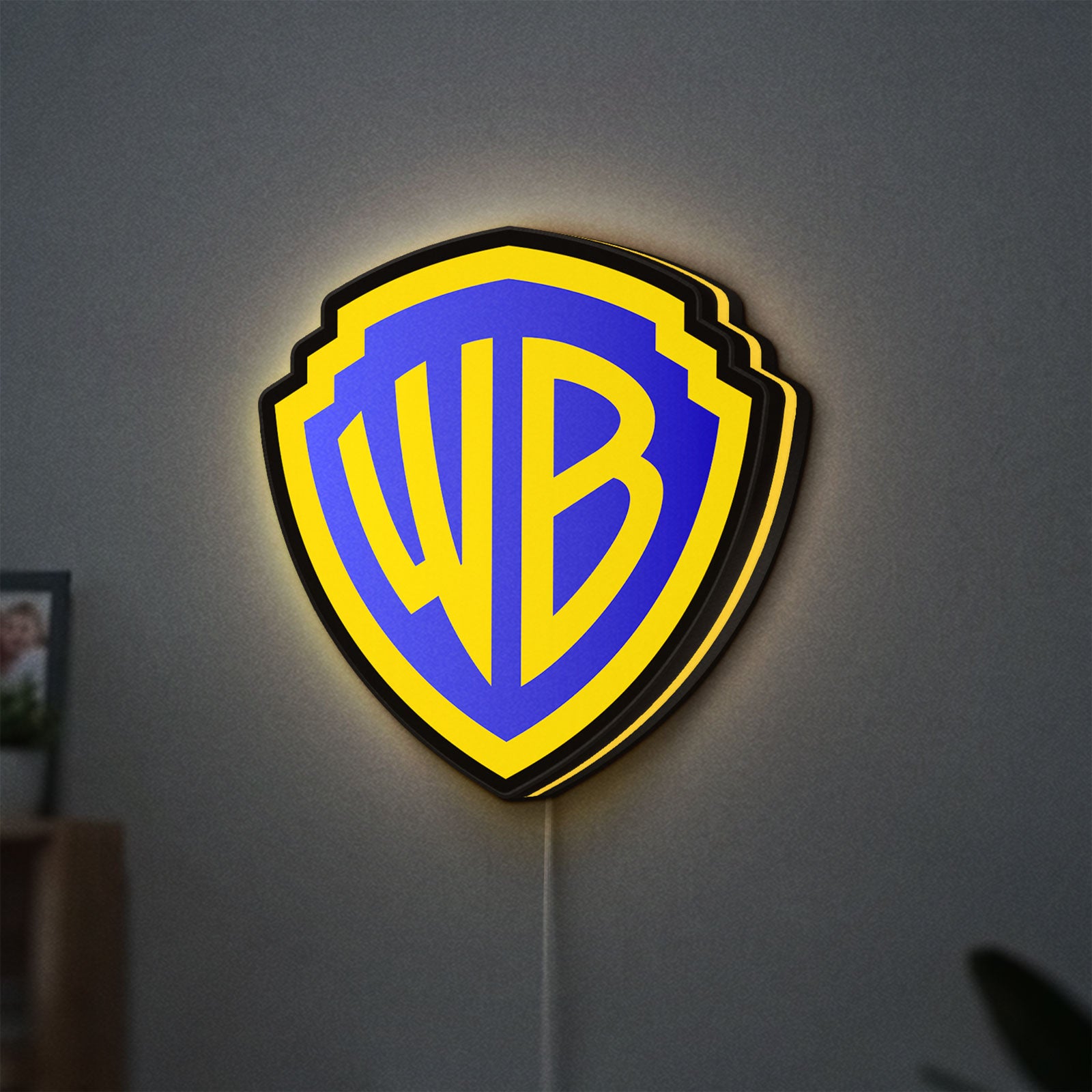 Warner Bros Shield LED lightbox hanging on a wall with yellow glow