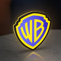 Warner Bros Shield LED lightbox standing on a desk from an angled side view with yellow glow
