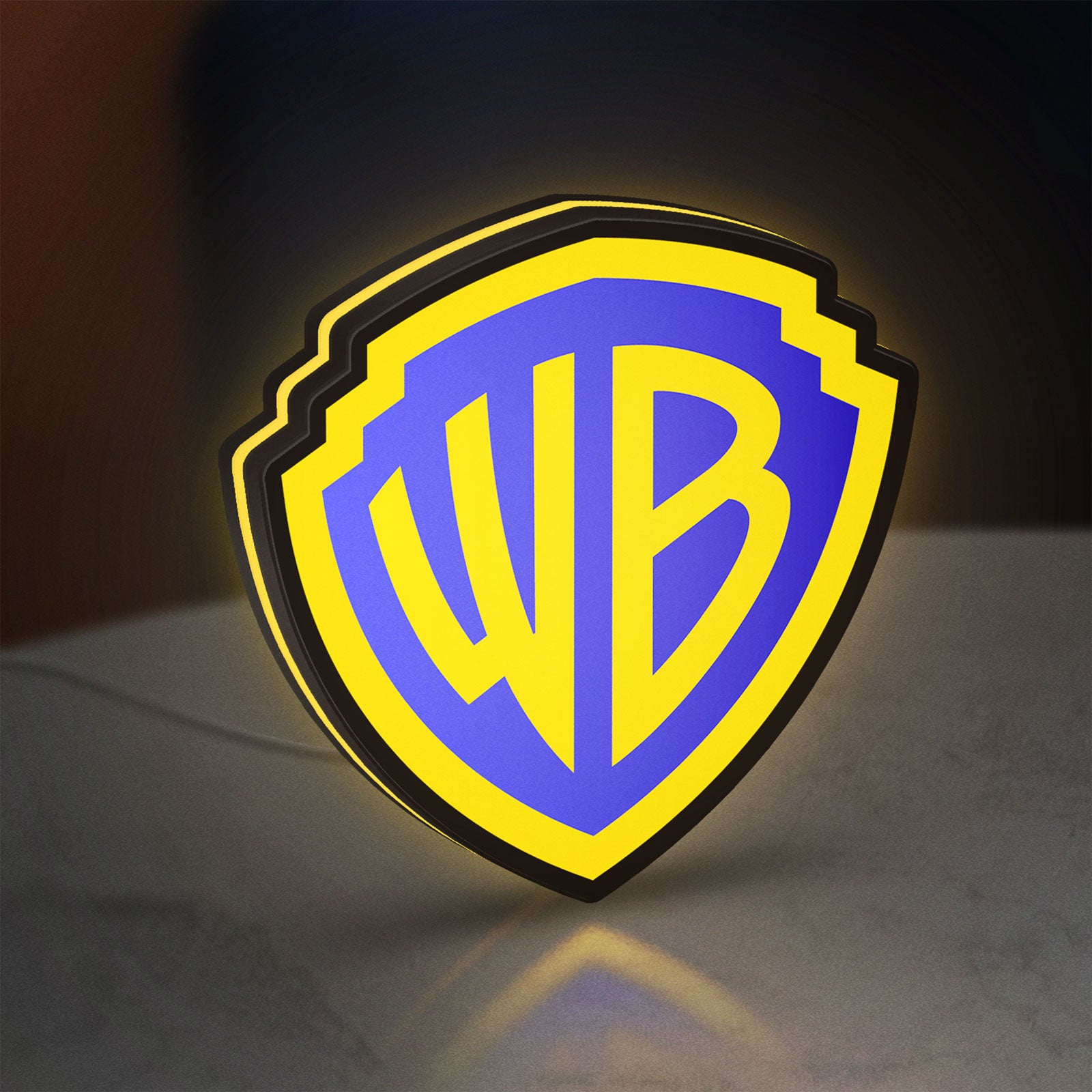 Warner Bros Shield LED lightbox standing on a desk from an angled side view with yellow glow