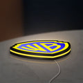 Warner Bros Shield LED lightbox lying flat on a desk with yellow glow