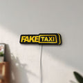 Unlit Fake Taxi LED lightbox mounted on a wall in daylight