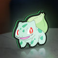 Bulbasaur LED lightbox standing on a desk from an angled side view with green glow