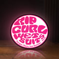 Front view of Rip Curl LED lightbox sign glowing on a wooden desk
