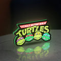Teenage Mutant Ninja Turtles LED lightbox standing on a desk from an angled side view with green glow