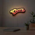 Cheers LED lightbox hanging on a room wall with soft yellow light