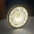 Battlestar Galactica Colonial Emblem LED lightbox standing on a desk from an angled side view with white glow