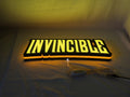 Invincible LED Sign (40cm) - Illuminated flat lay angled view, cool game room and bedroom decor