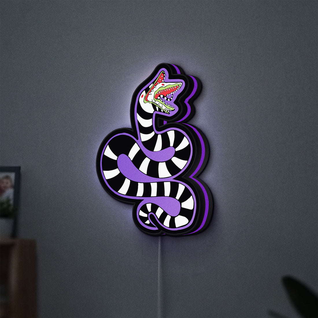 Beetlejuice Sandworm LED lightbox hanging on a wall with purple glow