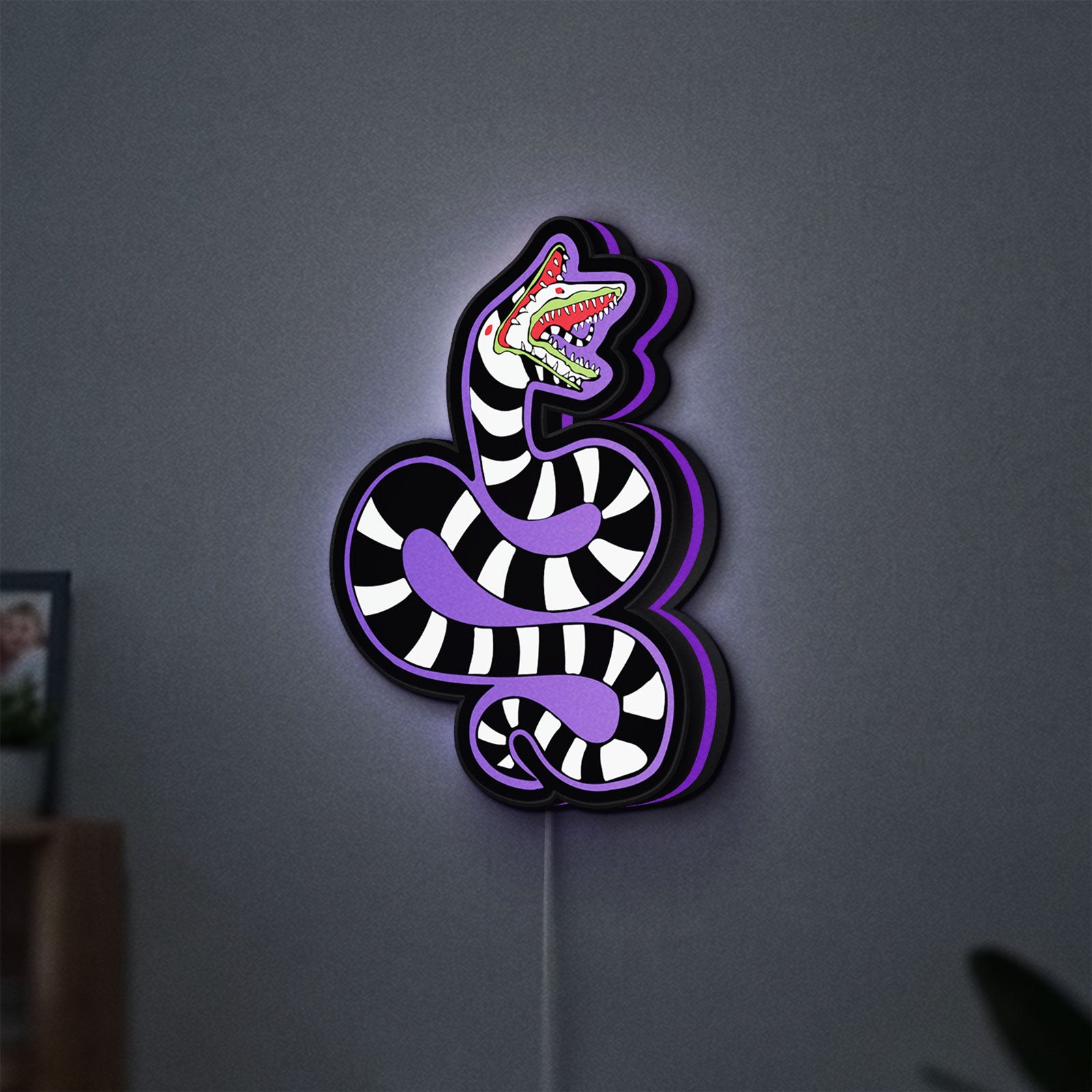 Beetlejuice Sandworm LED lightbox hanging on a wall with purple glow